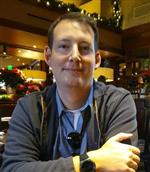 Headshot of Rob Woelich wearing a gray zip up sweatshirt and blue button up shirt
